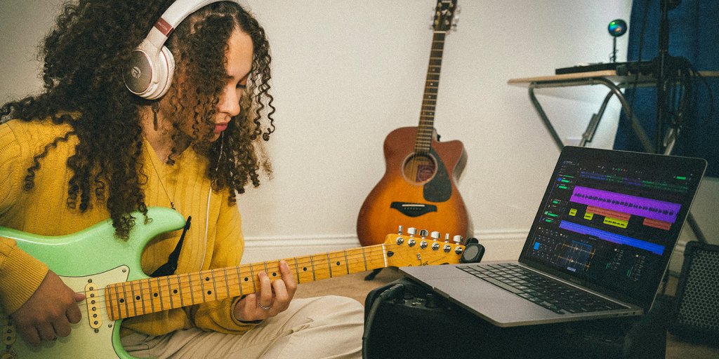 Music producer playing a guitar, seated next to an open laptop with Cakewalk Next software on the screen.